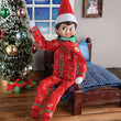 Load image into Gallery viewer, Scout Elf in red candy cane pajamas sitting on a small bed beside a decorated Christmas tree
