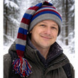 Load image into Gallery viewer, Man wearing a colorful striped hat and winter coat in a snowy forest.
