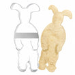 Load image into Gallery viewer, Pink bunny suit shaped stainless steel cookie cutter shown next to a freshly cut unbaked sugar cookie in the same bunny suit silhouette
